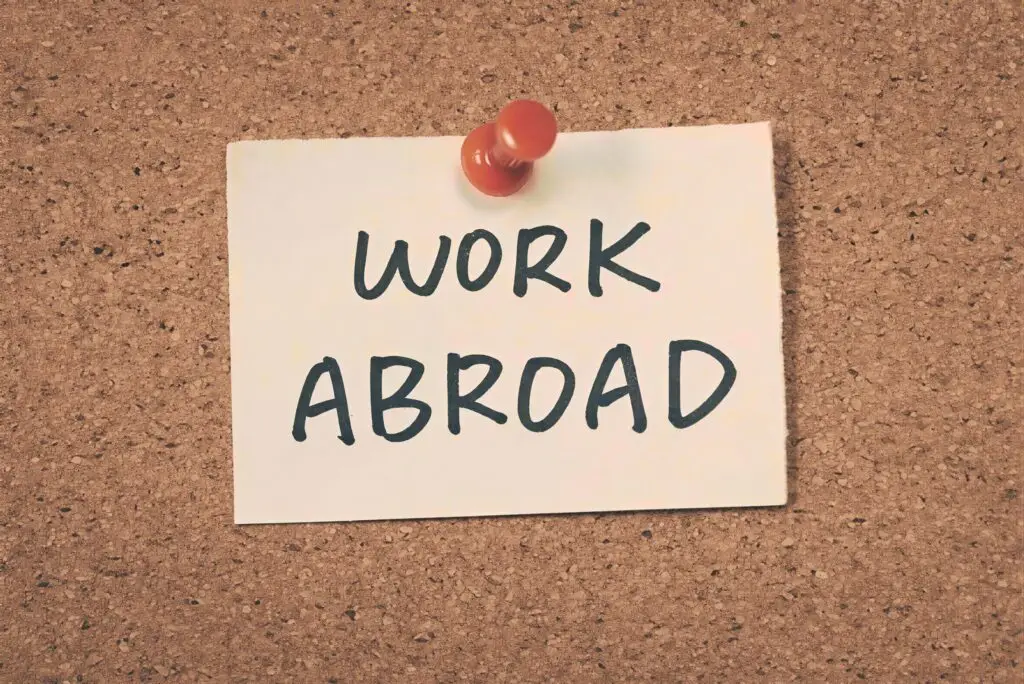 Cork bulletin board with paper pinned by red pushpin showing text ‘Work Abroad
