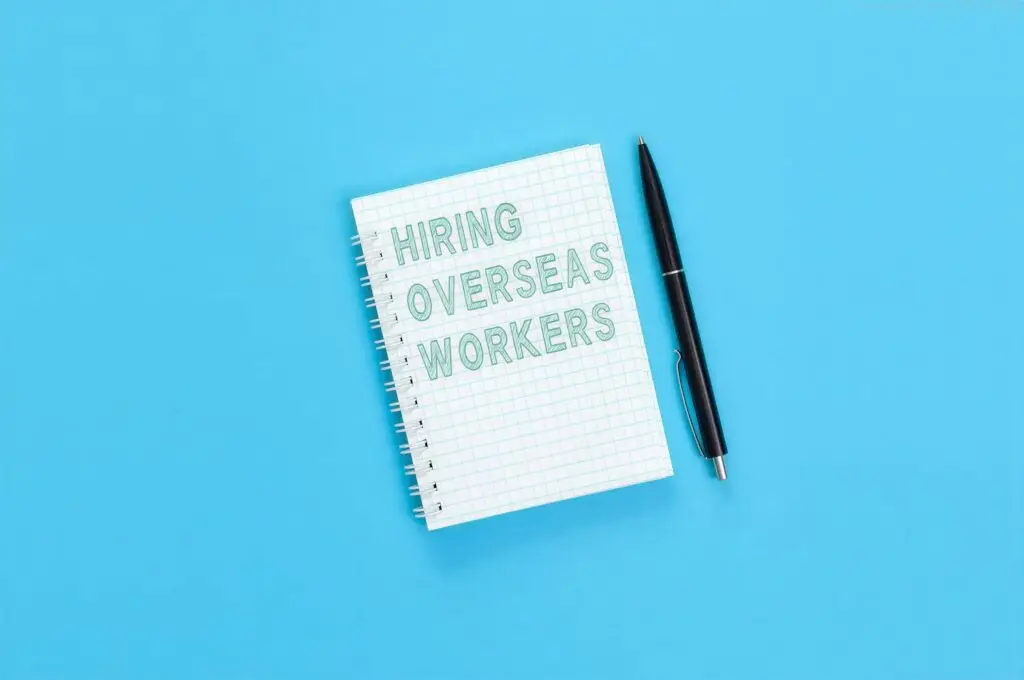 Notebook with text ‘Hiring Overseas Workers’ written in green outline, with pen on blue background